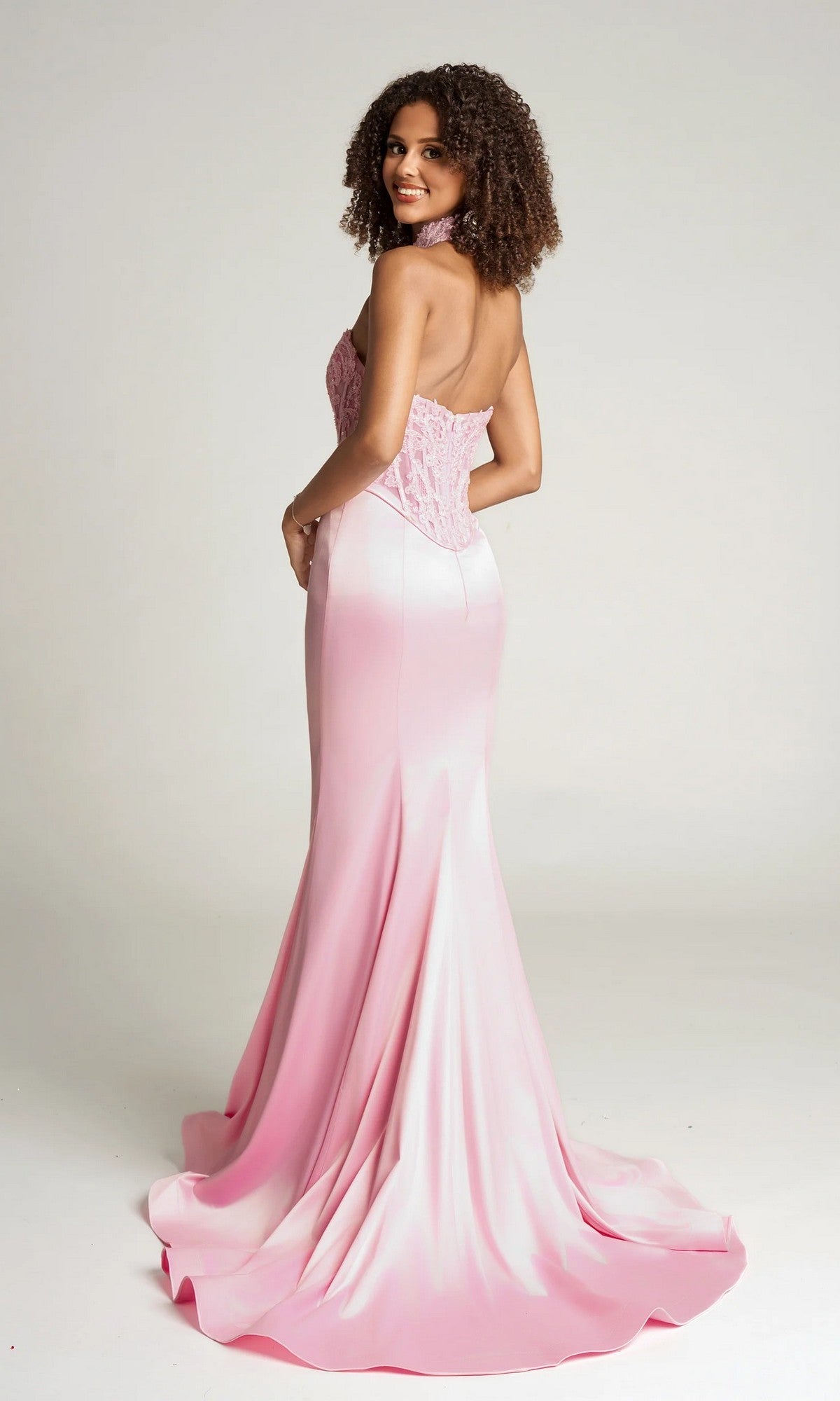 A woman models the Portia and Scarlett PS26086 long formal dress—a strapless, floor-length, light pink gown with a lace corset bodice—standing and looking over her shoulder against a plain background.